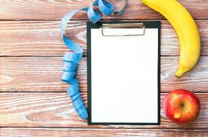 Note paper, measuring tape, banana and apple on a wooden background. Diet, meal plan. Healthy food concept. Flatlay. Top view. Copy space. photo