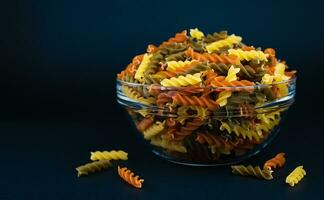 Italian tricolor organic fusilli paste in glass bowl on dark blue background. Close-up. Place for text. Selective focus. photo