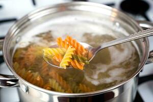 Italian tricolor fusilli paste is cooked in a pot on the stove. Cooking pasta. Healthy food concept. Selective focus. photo