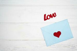 Love romantic message. Envelope with a red heart for Valentine's day on white wooden background. Flatlay. Top view. Place for text. photo