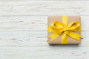 Holiday gift box wrapped in craft paper with colored bow on table background. Top view, flat lay, copy space photo