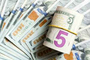 Top view of 5 rolled dollar bills on background made with one hundred dollar banknotes. Business concept photo