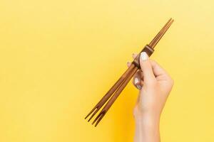 Female hand holding chopsticks on yellow background. Sushi concept with empty space for your idea photo