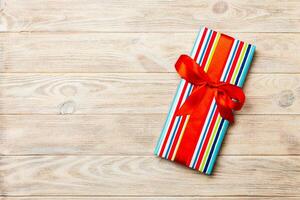 Beautiful gift box with a colored bow on the orange wooden table. Top view with copy space for you design. Christmas concept photo