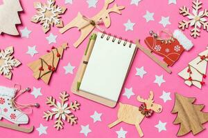 Top view of notebook, pink background decorated with festive toys and Christmas symbols reindeers and New Year trees. Holiday concept photo