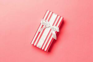 Top view Christmas present box with white bow on living coral background with copy space photo