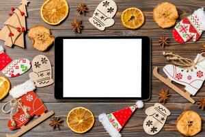 Top view of tablet on holiday wooden background. New Year decorations and toys. Christmas concept photo