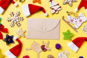 Top view of craft envelope with Christmas decorations and Santa hats on yellow background. Happy holiday concept photo