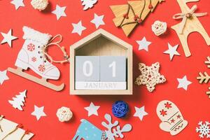 Top view of wooden calendar, holiday toys and decorations on red Christmas background. The first of January. New Year time concept photo