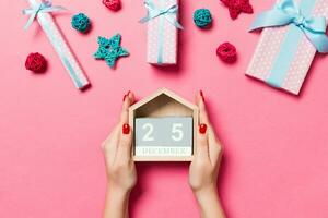 Top view of female hands holding calendar on pink background. The twenty fifth of December. Holiday decorations. Christmas time concept photo