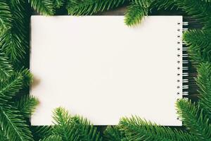 Top view of notebook decorated with a frame made of fir tree on wooden background. New Year time concept photo
