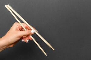 imagen creativa de palillos de madera en mano femenina sobre fondo negro. comida japonesa y china con espacio de copia foto