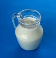 Glass jug of milk isolated on blue background, top view photo