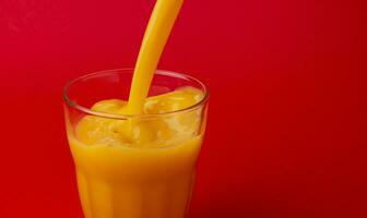 Orange juice pouring into glass, isolated on red background, with copy space photo