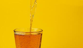 Apple juice pouring into glass, isolated on yellow background photo