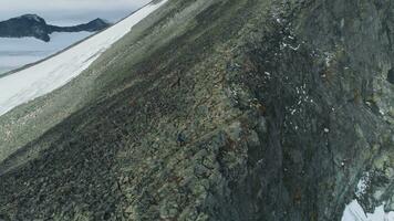 escursionista uomo è escursioni a piedi e ascendente nel nevoso montagne di Norvegia vicino il scogliera. aereo Visualizza. fuco è orbitante in giro a alto altitudine video