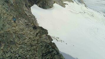 promeneur homme est randonnée et descendant près falaise dans neigeux montagnes de Norvège près falaise en utilisant en marchant poteaux. aérien voir. drone est en orbite autour video