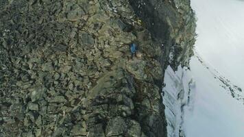 Wanderer Mann mit Gehen Stangen ist Stehen in der Nähe von Cliff im schneebedeckt Berge von Norwegen. Antenne Sicht. Drohne ist umkreisen um video