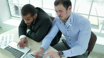 Two serious businessman working on a tablet and a laptop video