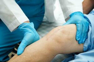 Doctor checking Asian elderly woman patient with scar knee replacement surgery in hospital. photo