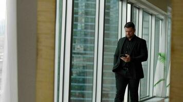 Businessman talking on a mobile phone. A businessman walks along the panoramic windows against the backdrop of skyscrapers. handsome businessman talking on a mobile phone in a modern office. photo