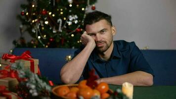 The guy is sitting at the festive New Year's table and is bored. A sad young man celebrates the New Year at home alone, sitting at the festive table. photo