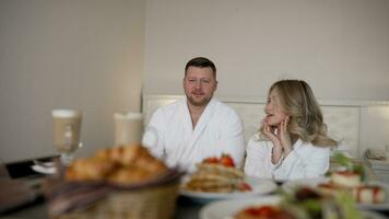 Service at the hotel, breakfast in the room. The guy appetizingly licks his lips at breakfast in the hotel. A guy and a girl in bathrobes at breakfast in a hotel room. photo