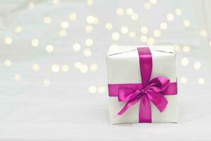 Decorative white gift box with a large barbie pink bow against a background bokeh of lights photo