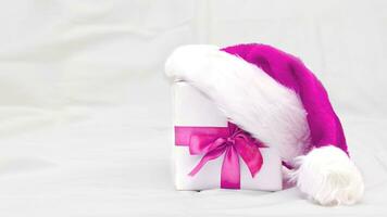 Decorative white gift box with a large barbie pink bow with santa hat on grey background photo