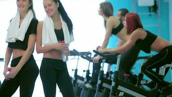 Girl look at each other and laugh in the gym while their friends do sports video