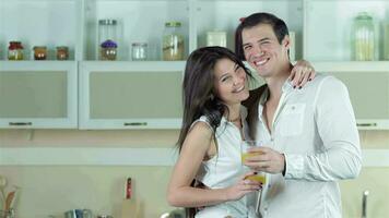 Couple standing at the kitchen table with vegetables smiling directly at the camera and she thumbs up video