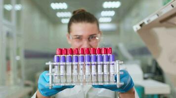 weiblich Wissenschaftler tragen Weiß Labor Mantel, Brille und Latex Handschuhe durchführen Wissenschaft Experiment. Frau hält im Hände Flasche mit ein transparent Flüssigkeit zum genetisch testen im Labor. video