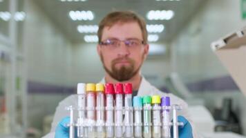 Scientist wearing white lab coat, goggles and latex gloves performing science experiment. Man holds in hands flask with a transparent liquid. video