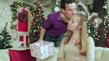 Loving couple dressed in sweater and scarf holding gifts in a Christmas furnished room video