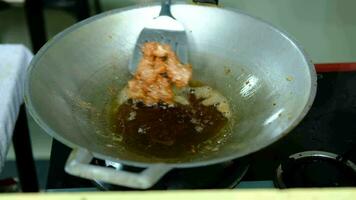 de kok handen maken een krat van frituren varkensvlees in een pan met heet olie. video