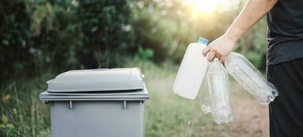 Person recycles plastic bottles in trash can photo