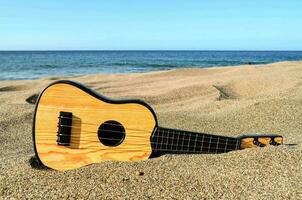 a ukulele sits on the sand near the ocean photo