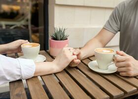 tradicional Pareja participación manos y café tazas en un de madera mesa. foto