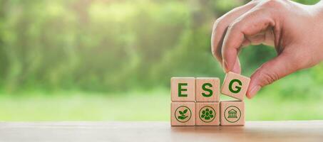 a hand placing the final block in a row of wooden blocks spelling out ESG, representing the concept of Environmental, Social, and Corporate Governance. photo