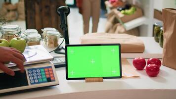 Greenscreen on device at cash register in local bio supermarket with locally grown produce, seller using isolated chromakey display on tablet. Business owner shows blank mockup screen. video