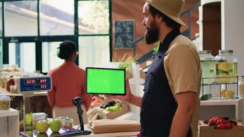 Storekeeper holds tablet with greenscreen in zero waste eco supermarket, using copyspace mockup on mobile gadget standing at checkout counter. Small business owner presents isolated display. video