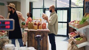 Shopper presents seasonings and products in glass jars to vegan customer while he is shopping for groceries. Middle eastern man wants to buy organic natural fresh fruits and veggies. video