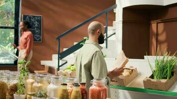 Client choosing bio produce to buy, approaching checkout counter to pay for bag filled with organic freshly harvested vegetables. Person going shopping for groceries at local natural market. video