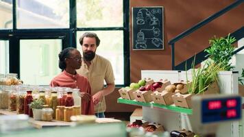 Clients asking about organic farming and fresh produce stored in crates at local zero waste eco market. Storekeeper presenting healthy eating alternatives to vegan couple shopping for groceries. video