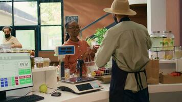 Seller weighting produce for woman, placing fruits and veggies on scale to ensure right price at local zero waste supermarket. Small business owner serving young client with groceries. video