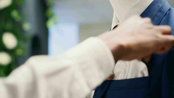 Extreme close up of employee tightens elegant blazer necktie on mannequin in luxurious clothing store. Worker adding pocket square on new collection stylish attire garment in premium fashion boutique video