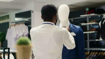 Mitarbeiter festziehen elegant Blazer Krawatte auf Mannequin im luxuriös Kleidung speichern. Arbeiter arrangieren Neu Sammlung stilvoll hoch Klasse Kleidung Kleider im Prämie Mode Boutique video