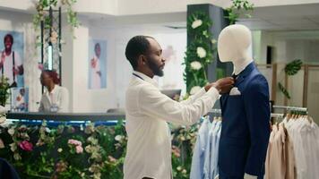 Employee in thrift shop arranging cheap and stylish blazer on mannequin. Retail assistant in second hand clothing store tidying up pocket square and lapels on formal attire garment video