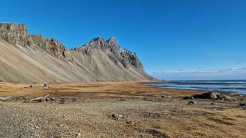 Nordic beach with massive rocky hills in amazing icelandic surroundings, vestrahorn mountains next to lands in Iceland. Stokksnes beachfront creating majestic landscape, ocean shoreline. photo