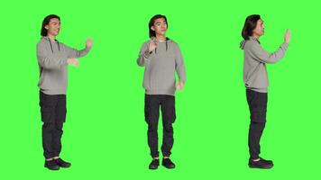 Adult doing okay gesture and showing disagreement at the same time, expressing positivity and negativity over full body greenscreen backdrop. Young man presenting good and bad symbol. video